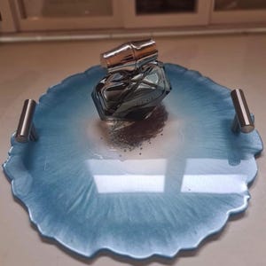 May include: A blue and white marbled resin tray with silver handles, holding a perfume bottle with a silver cap. The tray is a decorative item, perfect for displaying perfumes or other small objects. The tray's design is reminiscent of agate.