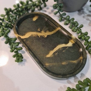 May include: A small oval tray with a dark green and gold marbled design. The tray is made of resin and has a smooth, glossy finish.
