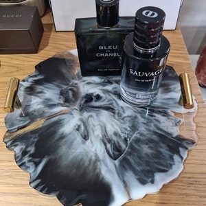 May include: A black and white resin tray with gold accents, featuring two bottles of men's cologne. The bottles are labelled "Bleu de Chanel" and "Sauvage Eau de Parfum".