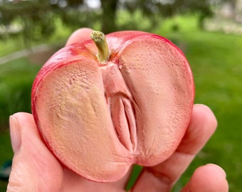 May include: A red apple cut in half, showing the inside of the fruit. The apple is held in a hand with a green background.