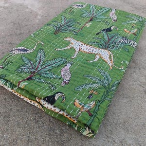 May include: Green quilt with a jungle design. The quilt features a leopard, toucans, parrots, and other birds amidst palm trees and foliage. The quilt is folded, showcasing the detailed stitching and the patterned border.