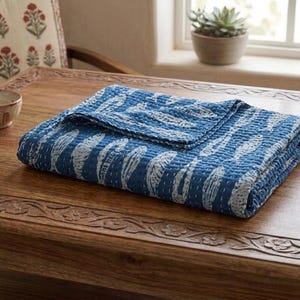 May include: A folded rectangular quilt featuring a deep blue background with a repeating white fish pattern. The fabric displays visible white running stitch details across the surface, creating a textured appearance throughout the textile piece.