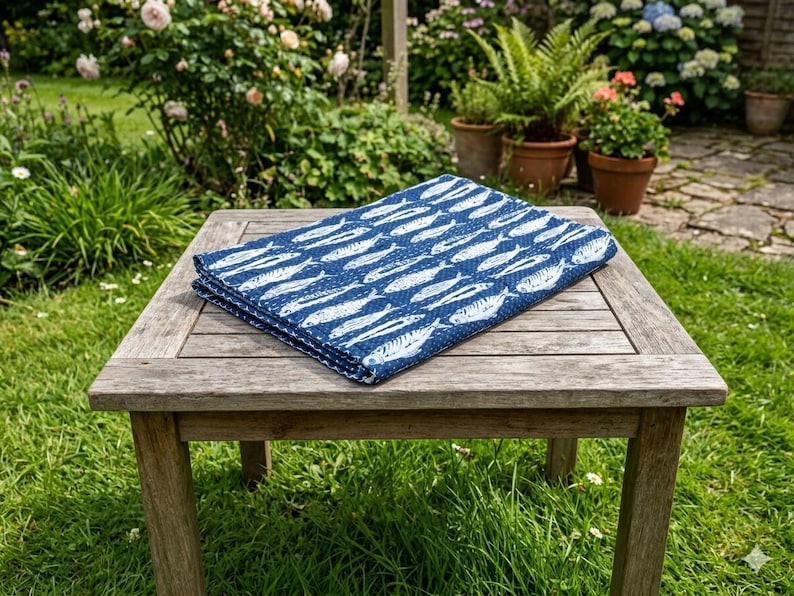 May include: A folded rectangular textile featuring a repeating pattern of white fish silhouettes on a dark blue background. The fabric has a visible quilted texture and is positioned flat on a square wooden table with a slatted surface design.