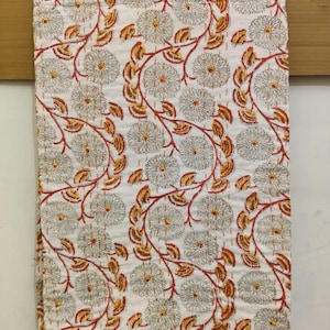 Könnte beinhalten: Weiße Baumwolldecke mit einem floralen Muster in Rot-, Orange- und Grautönen. Die Decke zeigt ein sich wiederholendes Muster aus stilisierten Blumen und Blättern.