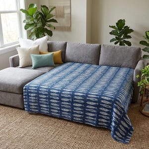 May include: A dark blue and white patterned throw blanket featuring a repeating fish motif draped over a gray sectional sofa. The blanket has a textured appearance with visible stitching and covers the main seating area of the sofa.
