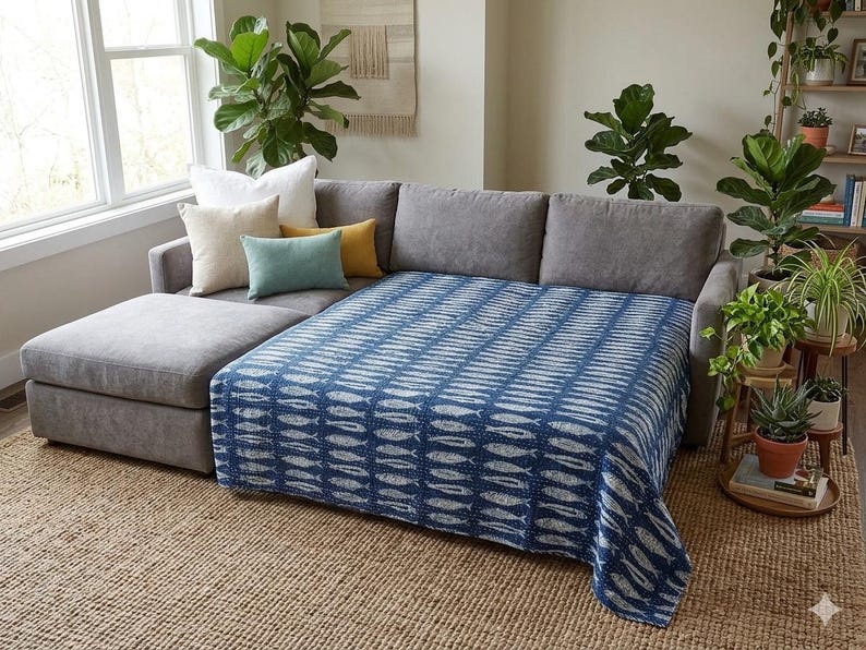 May include: A dark blue and white patterned throw blanket featuring a repeating fish motif draped over a gray sectional sofa. The blanket has a textured appearance with visible stitching and covers the main seating area of the sofa.