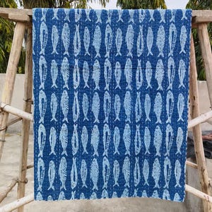 May include: A rectangular quilt featuring a repeating pattern of white fish printed on a deep blue background. The fabric displays visible white running stitch details throughout the surface, creating a textured, quilted appearance across the textile.