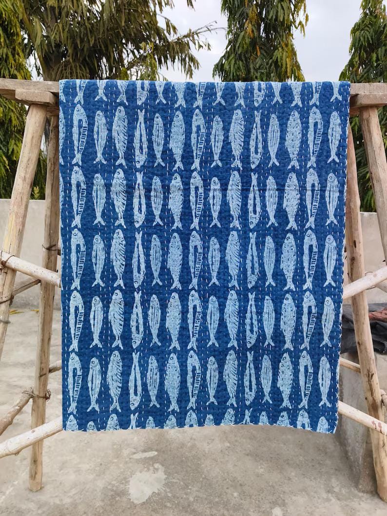 May include: A rectangular quilt featuring a repeating pattern of white fish printed on a deep blue background. The fabric displays visible white running stitch details throughout the surface, creating a textured, quilted appearance across the textile.