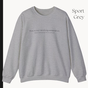 K&ouml;nnte beinhalten: Ein grauer Sweatshirt mit dem Text "This is my writing sweatshirt. Easily distracted. Do not disturb." auf der Vorderseite.
