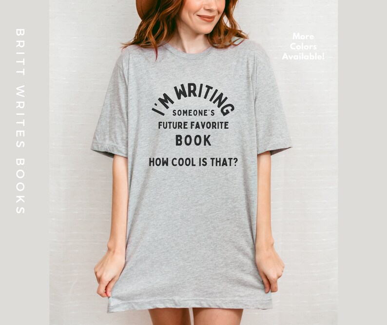 Peut inclure: T-shirt gris avec un texte noir qui dit "J'&eacute;cris le futur livre pr&eacute;f&eacute;r&eacute; de quelqu'un. C'est cool, non ?"