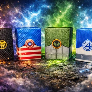Könnte beinhalten: Vier rechteckige Deckboxen mit Superhelden-Motiven. Die erste ist schwarz mit einem goldenen Panther-Emblem. Die zweite ist blau und rot mit einem Sternenschild. Die dritte ist grün und silber mit einem schwarzen Symbol. Die vierte ist blau und weiß mit einer 4.
