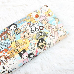 May include: A colorful fabric with a repeating pattern of cartoon characters and designs. The fabric features a variety of characters, including a skull, a bear, a dog, and a woman in a swimsuit. The fabric also features text, including "Toki-Doki", "Route 66", and "Adios".