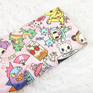 May include: Pink fabric with a repeating pattern of cartoon characters and objects. The characters include a unicorn, a cactus, a juice box, a sushi roll, and a monster. The objects include a fan, a candy cane, and a star.