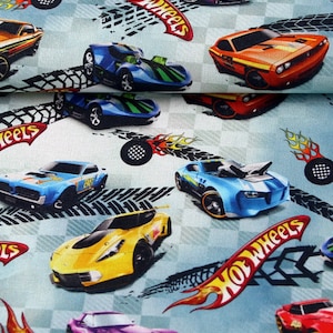 May include: A blue and white fabric with a repeating pattern of Hot Wheels cars and the Hot Wheels logo. The cars are in various colours, including red, yellow, blue, and purple. The background is a light blue with a chequered pattern.