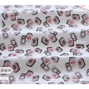 May include: White fabric with a repeating pattern of green and red mahjong tiles. The tiles have Chinese characters on them. The fabric is 2.5 inches wide.