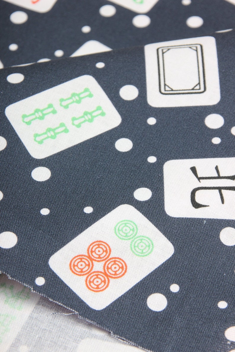 Pu&ograve; includere: Un tessuto blu scuro con uno sfondo bianco a motivi di tessere di mahjong. Le tessere hanno vari simboli e numeri. Il tessuto &egrave; punteggiato da cerchi bianchi.