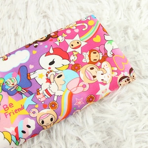 Op de afbeelding: Paarse en roze stof met een herhalend patroon van cartoonfiguren, regenbogen, sterren en donuts. De tekst "Be Friend" is zichtbaar in de linkerbenedenhoek.