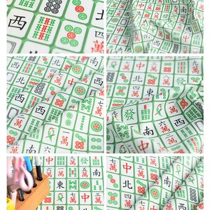 May include: White fabric with a repeating pattern of green mahjong tiles. The tiles feature Chinese characters and symbols, including the numbers one through nine, the characters for East, South, West, North, and the wind symbols. The fabric is perfect for crafting projects, such as making bags, pillows, or quilts.