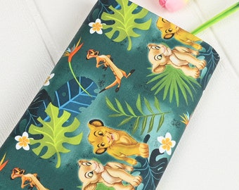 May include: Green fabric with a repeating pattern of cartoon lions and meerkats in a jungle setting. The lions are orange and brown with green eyes. The meerkats are brown with black eyes. The jungle is green with yellow flowers.