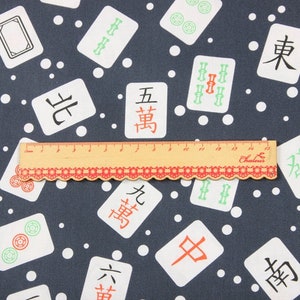Pu&ograve; includere: Un tessuto blu scuro con un motivo a pois bianchi e un motivo ripetuto di tessere di mahjong bianche con caratteri cinesi e simboli di bamb&ugrave; verdi. Un righello &egrave; posizionato sopra il tessuto.