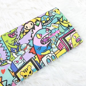 May include: A colorful fabric with a cartoon design featuring monsters, robots, and other whimsical characters. The fabric is printed with a variety of bright colors, including pink, blue, yellow, green, and orange.