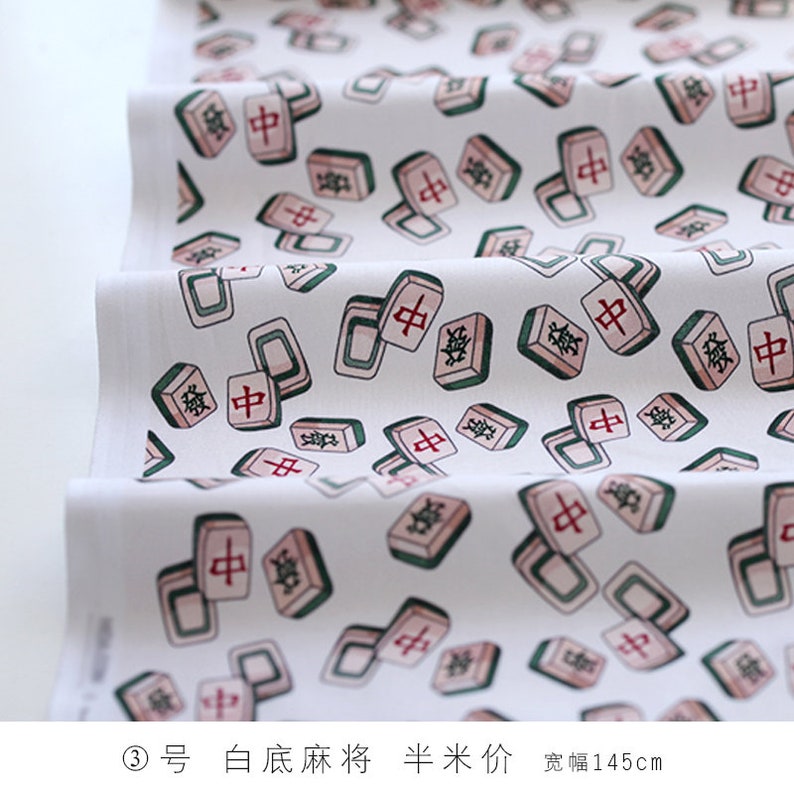 May include: White fabric with a repeating pattern of pink and green mahjong tiles. The tiles have Chinese characters on them. The fabric is 145 cm wide.