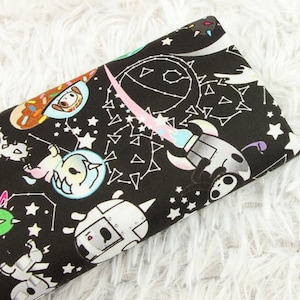 May include: Black fabric with a white and colourful print of space-themed characters, including a unicorn, a rocket, and a robot. The fabric is covered in white stars and constellations.