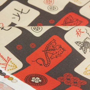 May include: Close-up of fabric with a repeating pattern of red, white, and black Mahjong tiles. The tiles feature various symbols and Chinese characters. The fabric is folded, revealing a white edge.