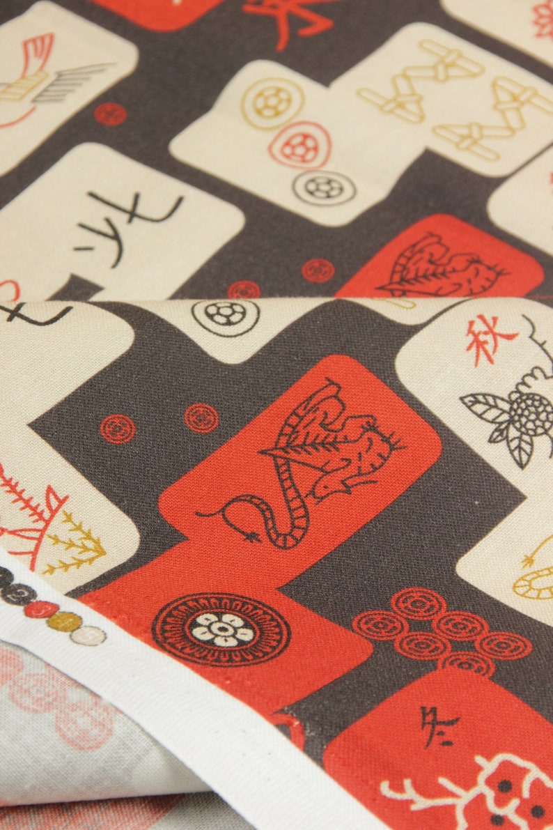 May include: Close-up of fabric with a repeating pattern of red, white, and black Mahjong tiles. The tiles feature various symbols and Chinese characters. The fabric is folded, revealing a white edge.