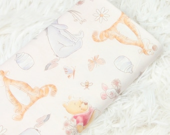 May include: A pink fabric with a repeating pattern of Winnie the Pooh and his friends, including Tigger, Piglet, and Eeyore. The characters are depicted in a watercolor style with soft colors.