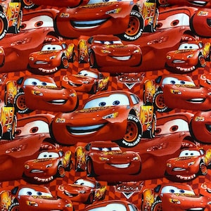 May include: Red fabric with a repeating pattern of cartoon racing cars. The cars are red with black accents and have a smiling face with blue eyes. The background is a red and white chequered pattern.