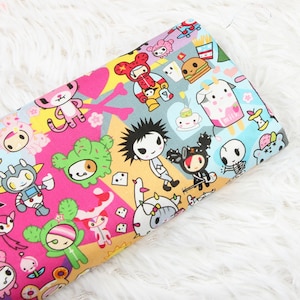 May include: A pink and yellow fabric with a repeating pattern of cartoon characters, including a robot, a cow, a cactus, and a skull. The fabric has a white background with a variety of colours and patterns.