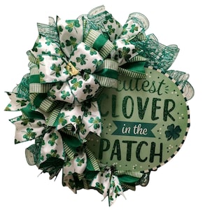 May include: A green and white wreath with a sign that says "Cutest Clover in the Patch". The wreath is decorated with green and white ribbon and shamrocks.