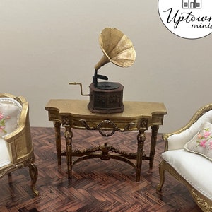 May include: A miniature dollhouse living room set featuring a gold-painted console table, two white chairs with floral cushions, and a vintage gramophone with a gold horn.
