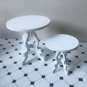 May include: Two white miniature tables with ornate legs. The larger table is 10 inches in diameter and the smaller table is 6 inches in diameter. Both tables have a white painted finish.