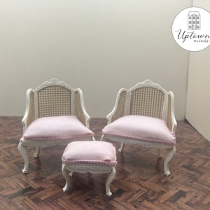 Puede incluir: Un conjunto de tres sillas blancas en miniatura con cojines rosas. Las sillas tienen un respaldo de caña tejido y están decoradas con un borde delicado. Las sillas están dispuestas sobre un suelo de madera con un patrón de tablero de ajedrez.