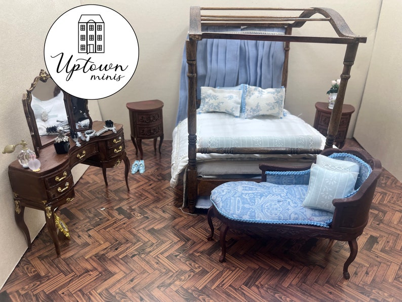 May include: A miniature dollhouse bedroom set with a canopy bed, a vanity with a mirror, two nightstands, and a chaise lounge. The bed is made with blue and white bedding, and the chaise lounge is covered in a blue and white paisley fabric. The furniture is made of wood and has a dark brown finish.