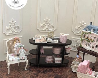May include: A miniature room scene featuring a white chair with a floral cushion, two dolls, a dark wood console table with open books and round boxes, a dollhouse, and a pink doll carriage. The wall features white molding and a logo reading UPTOWN MINIS EST 2021 CRAFTING HAPPINESS.