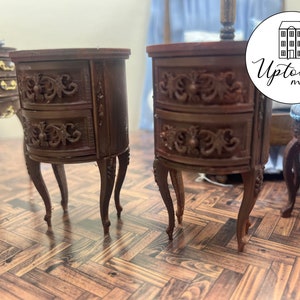 May include: Two brown wooden nightstands with ornate carvings and two drawers each. The nightstands have curved fronts and stand on four legs. The nightstands are on a wood floor.