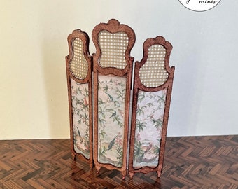 May include: A three-panel room divider made of wood with a woven cane back and floral patterned fabric panels. The divider is painted in a brown color and has a distressed finish. The divider is standing on a wooden floor.