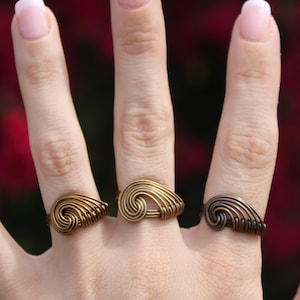 May include: Three gold-toned rings with a spiral design. The rings are worn on the middle, ring, and pinky fingers of a hand.