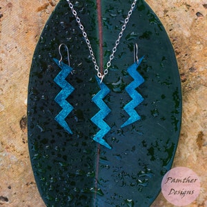 Könnte beinhalten: Ein Set mit blauen Blitzarmbändern und einer passenden Halskette. Der Schmuck ist aus Metall und hat eine strukturierte Oberfläche. Der Schmuck wird auf einem grünen Blatt mit Wassertropfen präsentiert.