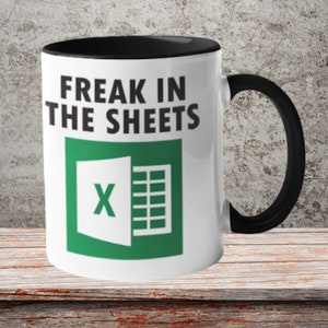 May include: White coffee mug with a black rim and handle. The mug features a green Microsoft Excel logo and the text "Freak in the sheets".