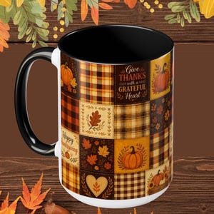 May include: A ceramic mug with a black handle and interior, featuring a patchwork design of autumn-themed squares including plaid patterns, pumpkins, oak leaves, and hearts. The text "Give THANKS with a GRATEFUL HEART" is printed on the front.