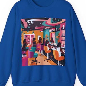 May include: A blue sweatshirt with a colorful illustration of a nail salon with women getting their nails done. The salon has a pink, yellow, and green color scheme.