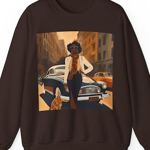 May include: A brown sweatshirt with a graphic print of a woman in a white jacket and sunglasses standing next to a vintage car in a city street.