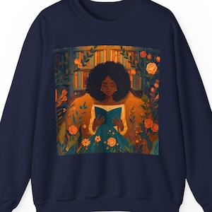 May include: Navy blue sweatshirt featuring a vibrant illustration of a person reading a book surrounded by flowers and a bookshelf. The artwork is in warm tones of orange, yellow, and green, creating a cozy and inviting scene. The sweatshirt is a comfortable, casual style.