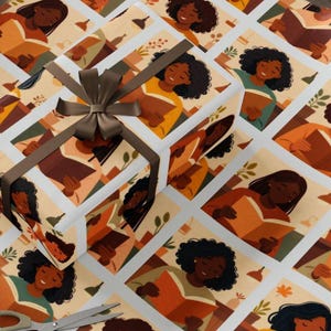 May include: Gift-wrapped box and wrapping paper featuring a repeating pattern of people reading books. The illustrations are in shades of brown, orange, and cream. A brown ribbon and bow adorn the gift box. Scissors and tape are also visible.