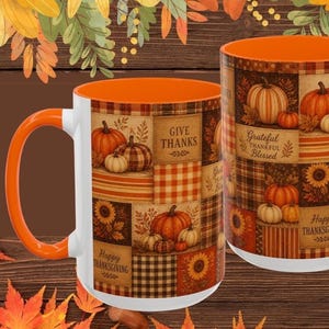 May include: Two ceramic mugs with bright orange interiors and handles. The exterior features a patchwork design of autumn-themed squares, including pumpkins, sunflowers, plaid patterns, and text that reads Give Thanks, Grateful Thankful Blessed, and Happy Thanksgiving.