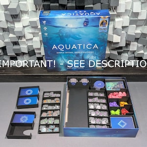 以下が含まれることがあります： 青と白の海のテーマの「Aquatica」というタイトルのボードゲームボックス。ボックスは開いており、カード、トークン、ミニチュアフィギュアなど、黒いトレイに入ったゲームコンポーネントが表示されています。「IMPORTANT! - SEE DESCRIPTION」というテキストが表示されています。